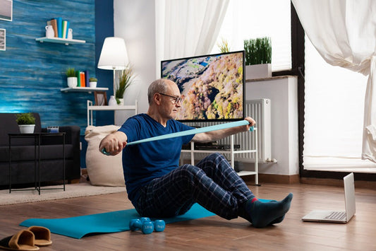 pensioner working body resistance exercising arms muscles using elastic band sitting on yoga mat